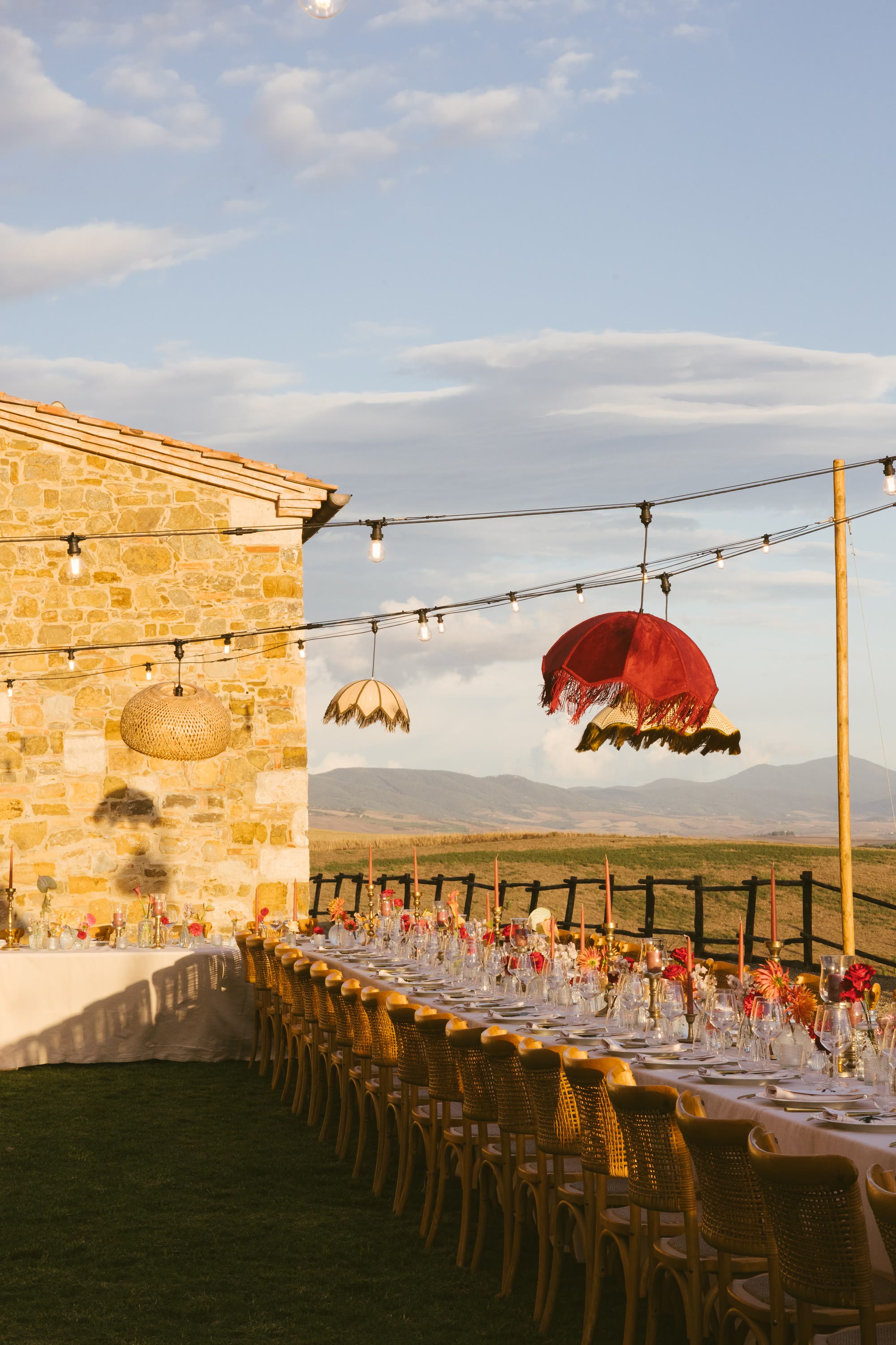 Parasol lanterns over a long laid table on a stone terrace, the hills behind