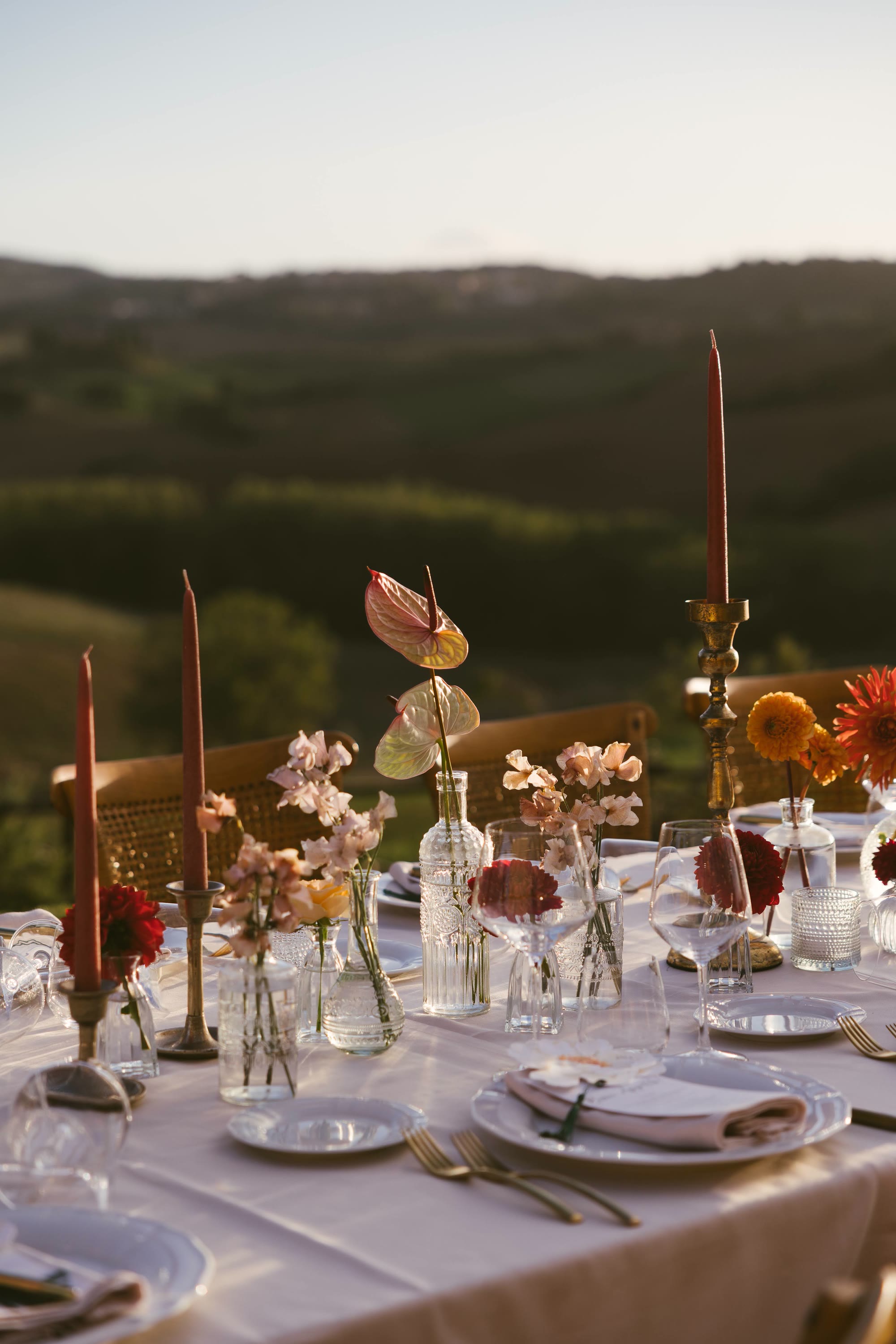 Una tavola apparecchiata con fiori e candele, dietro le colline della Val d'Orcia