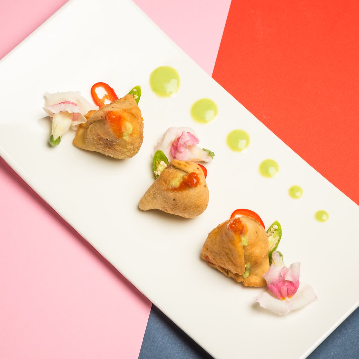 Three samosas on a white plate with dots of green chutney